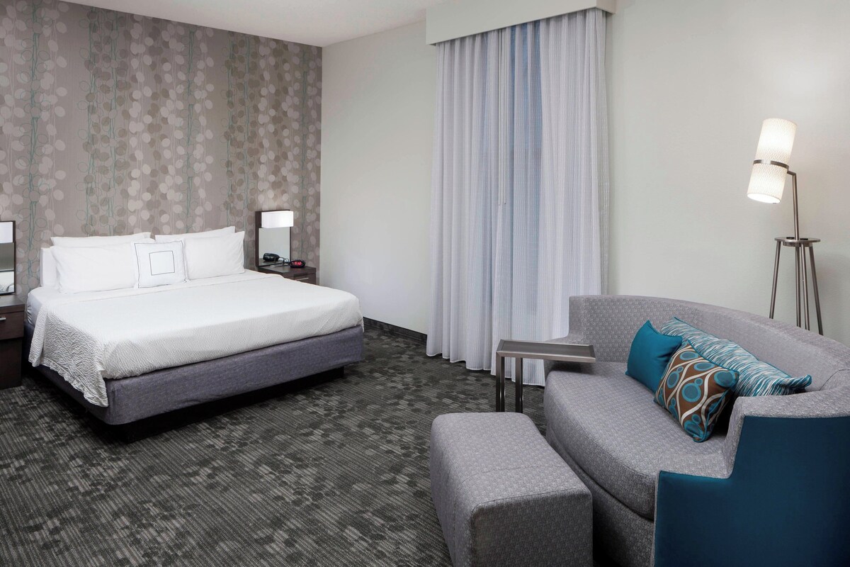 A hotel room with a bed, a sofa, a small table, and a lamp.