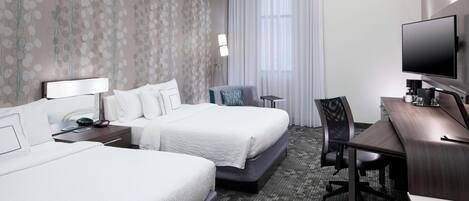 Une chambre d’hôtel avec deux lits, un bureau, une chaise, une télévision et une lampe.