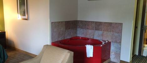 Una habitación de hotel con una bañera de hidromasaje roja, un sillón color beige y un cuadro en la pared.