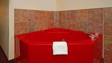 A red bathtub with a white towel, tiled walls, and a corner shower area.