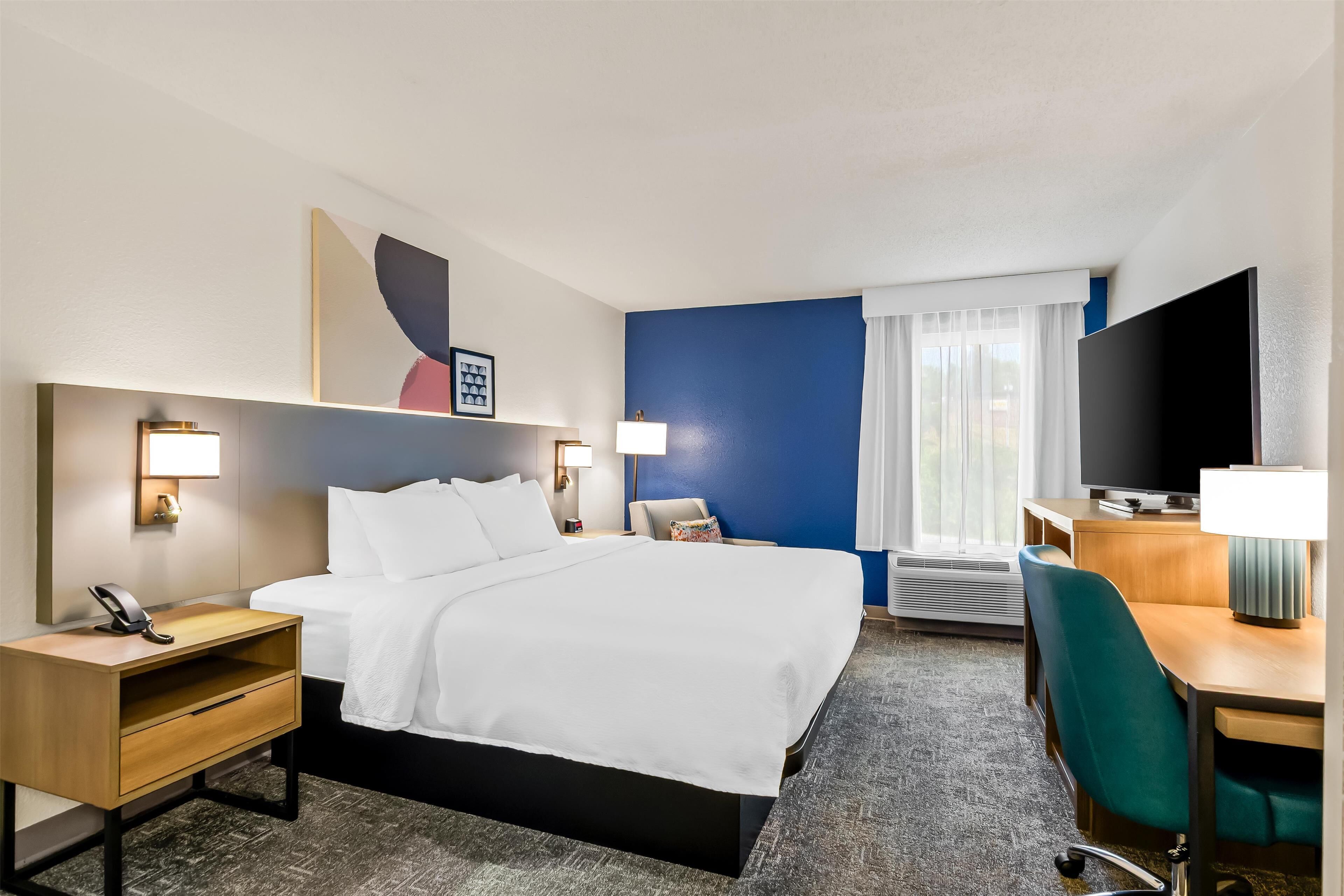 Habitación de hotel con cama, mesitas de noche, escritorio, silla, televisor y ventana con cortinas.