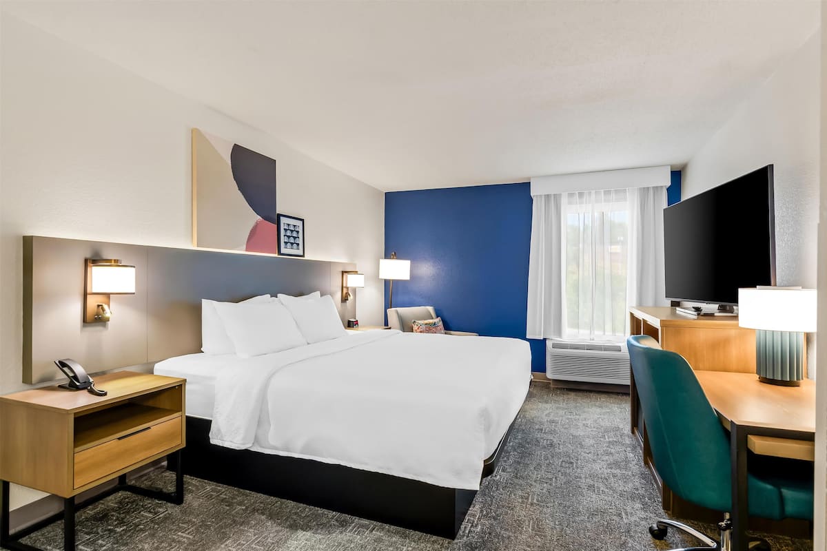 Habitación de hotel con cama, mesitas de noche, escritorio, silla, televisor y ventana con cortinas.