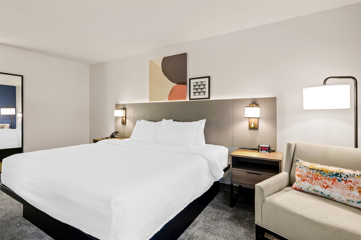 A hotel room with a large bed, bedside tables, a desk, a chair, and wall-mounted lamps.