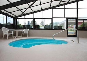 An indoor swimming pool with a glass ceiling, two white chairs, and a view of the outdoors.