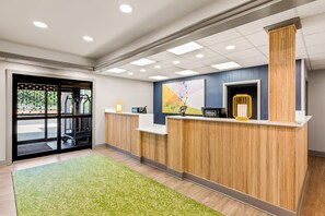 A hotel reception area with a wooden reception desk, a digital screen, and a telephone.