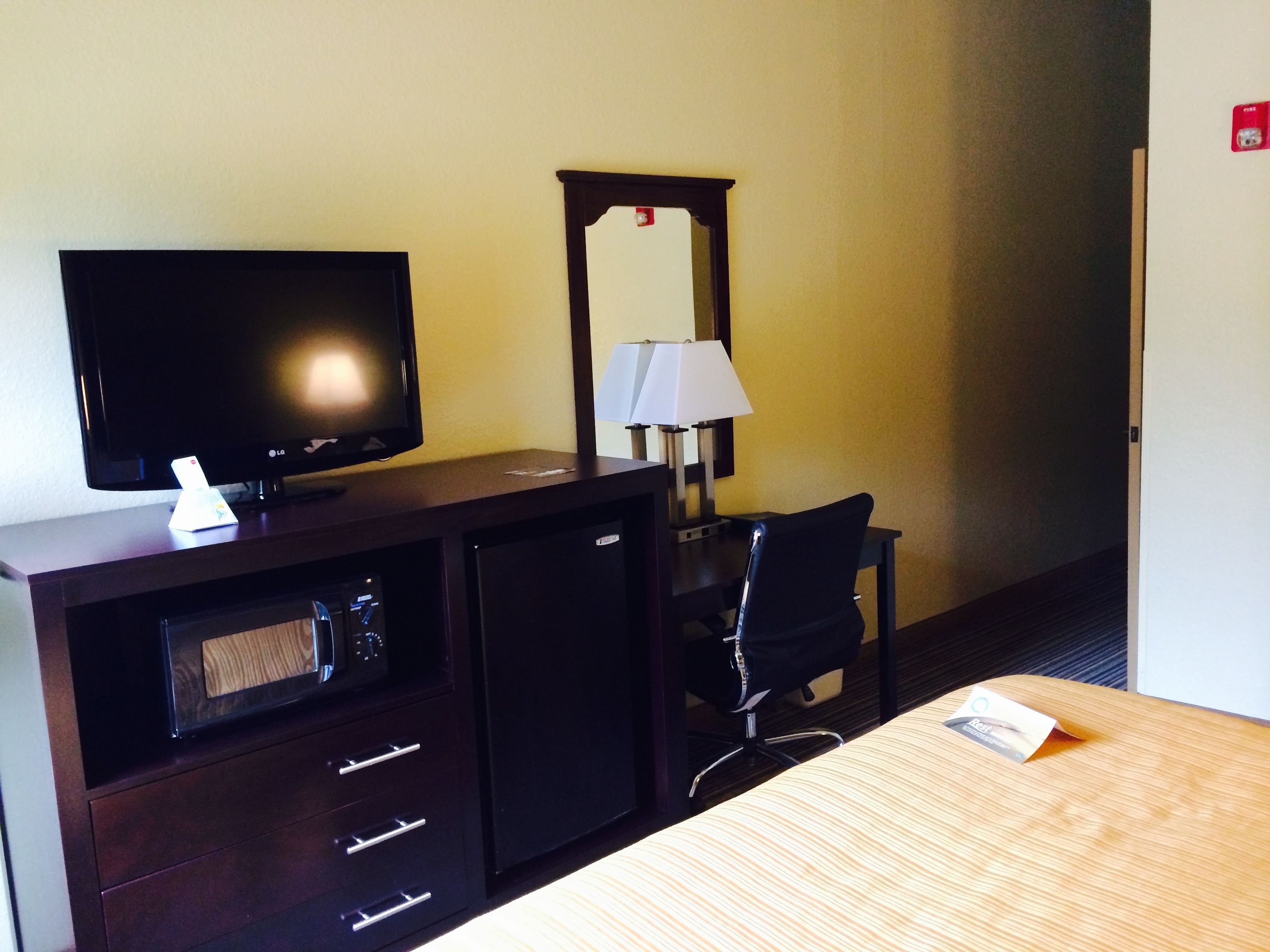 Een hotelkamer met een televisie, bureau, stoel, lamp en een minibar.