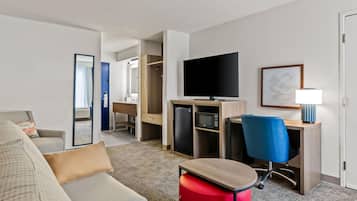 Una camera d'hotel con un divano, una scrivania con un computer, una televisione, un forno a microonde e una sedia.