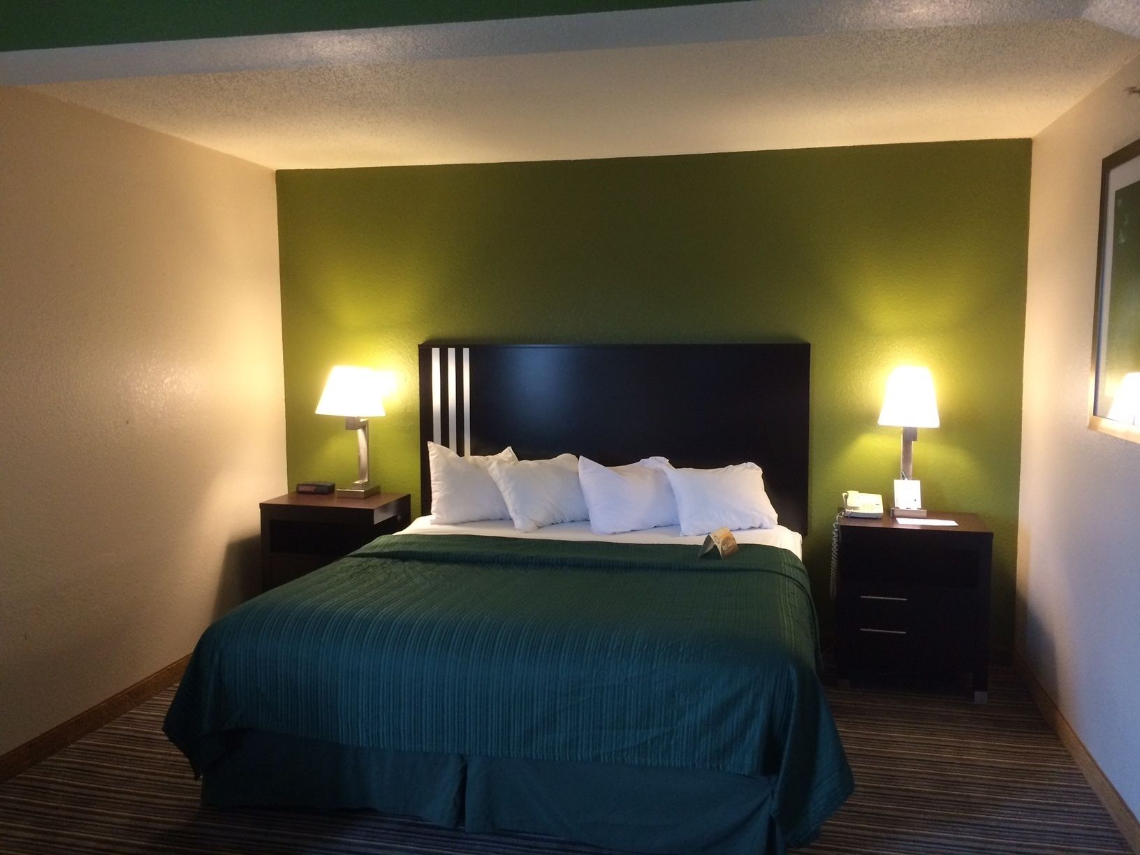 A hotel room with a large bed, two bedside tables, and green walls.