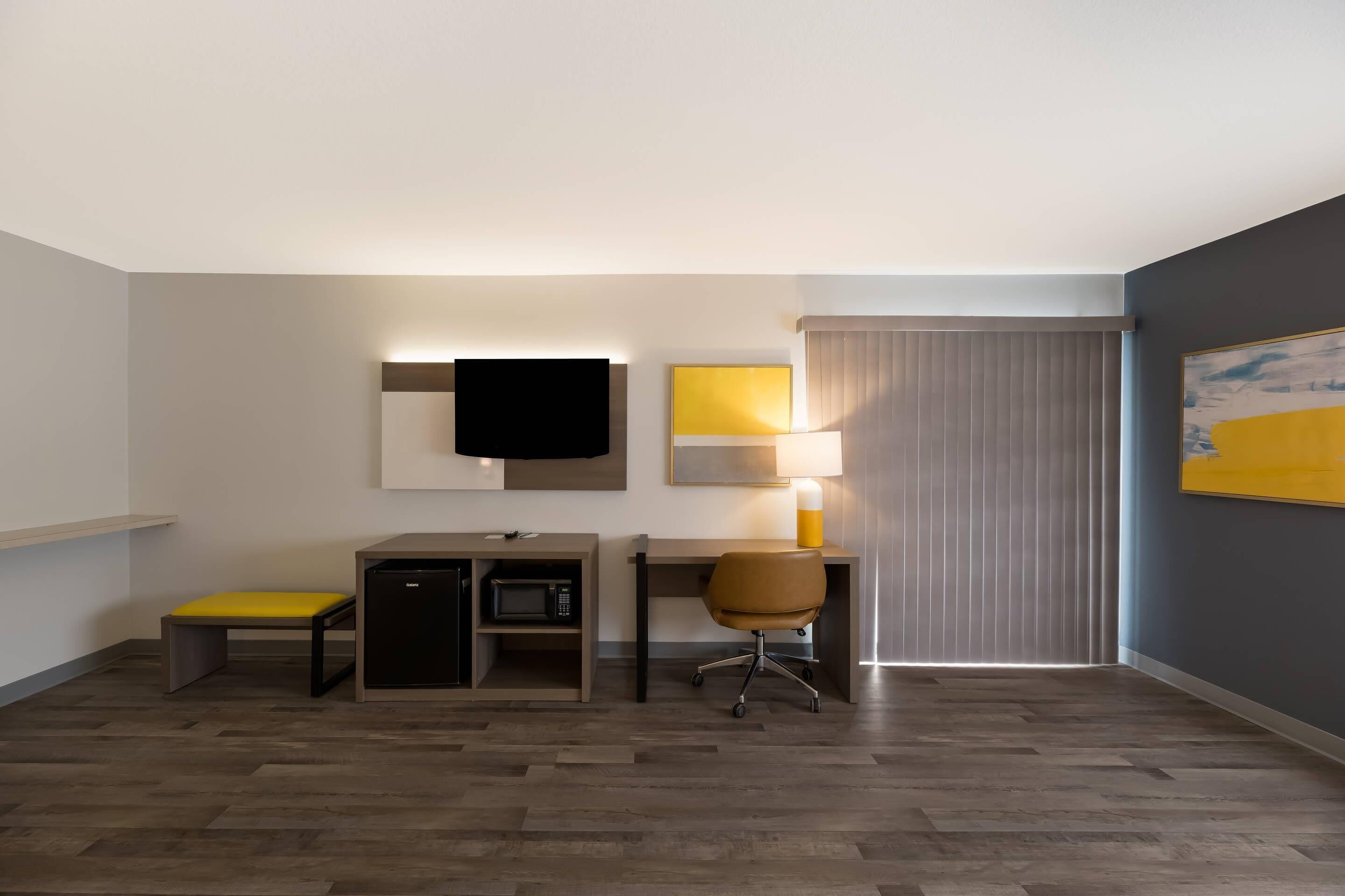 Une chambre d’hôtel équipée d’un bureau, d’une chaise et d’un téléviseur à écran plat fixé au mur.
