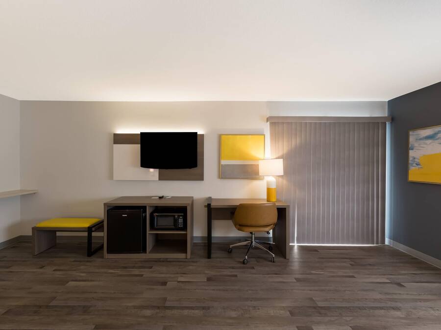 A hotel room with a desk, chair, and a flat-screen TV mounted on the wall.