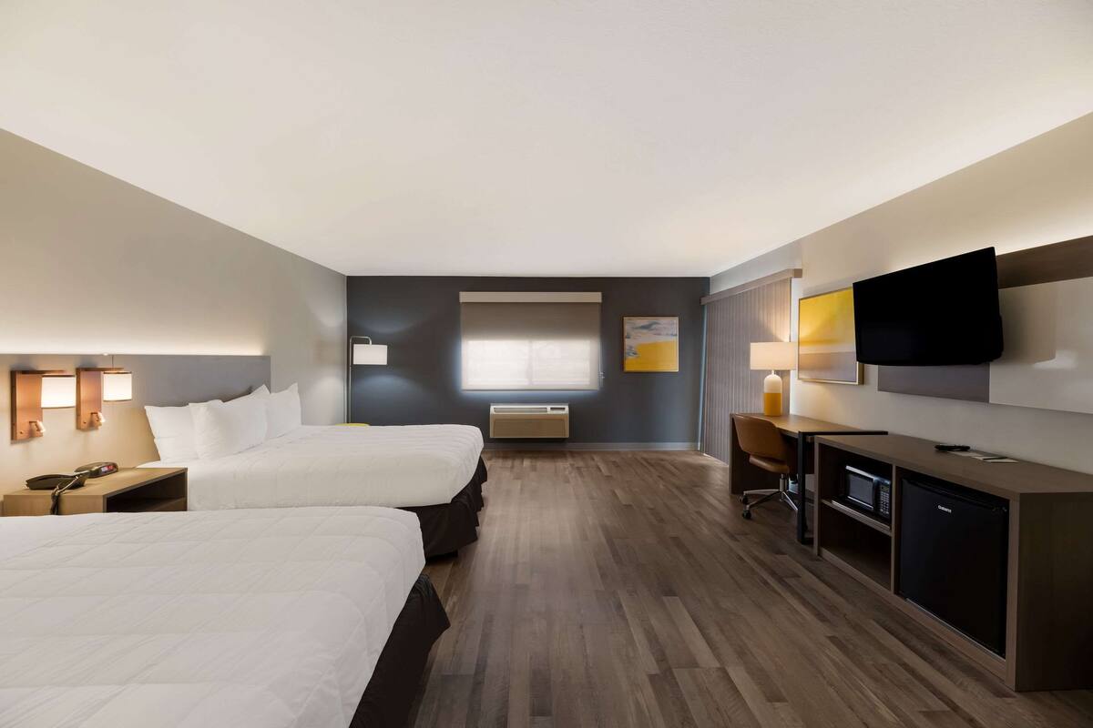 A hotel room with two beds, a desk, a television, and a microwave.