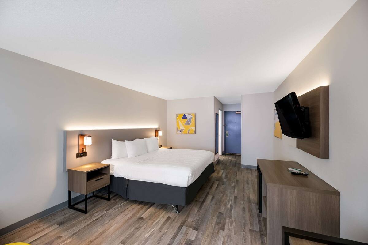 A modern hotel room with a large bed, bedside tables, a flat-screen TV, and a small desk.