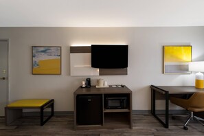 A hotel room with a bed, a desk, a chair, a coffee maker, a microwave, and artwork on the walls.