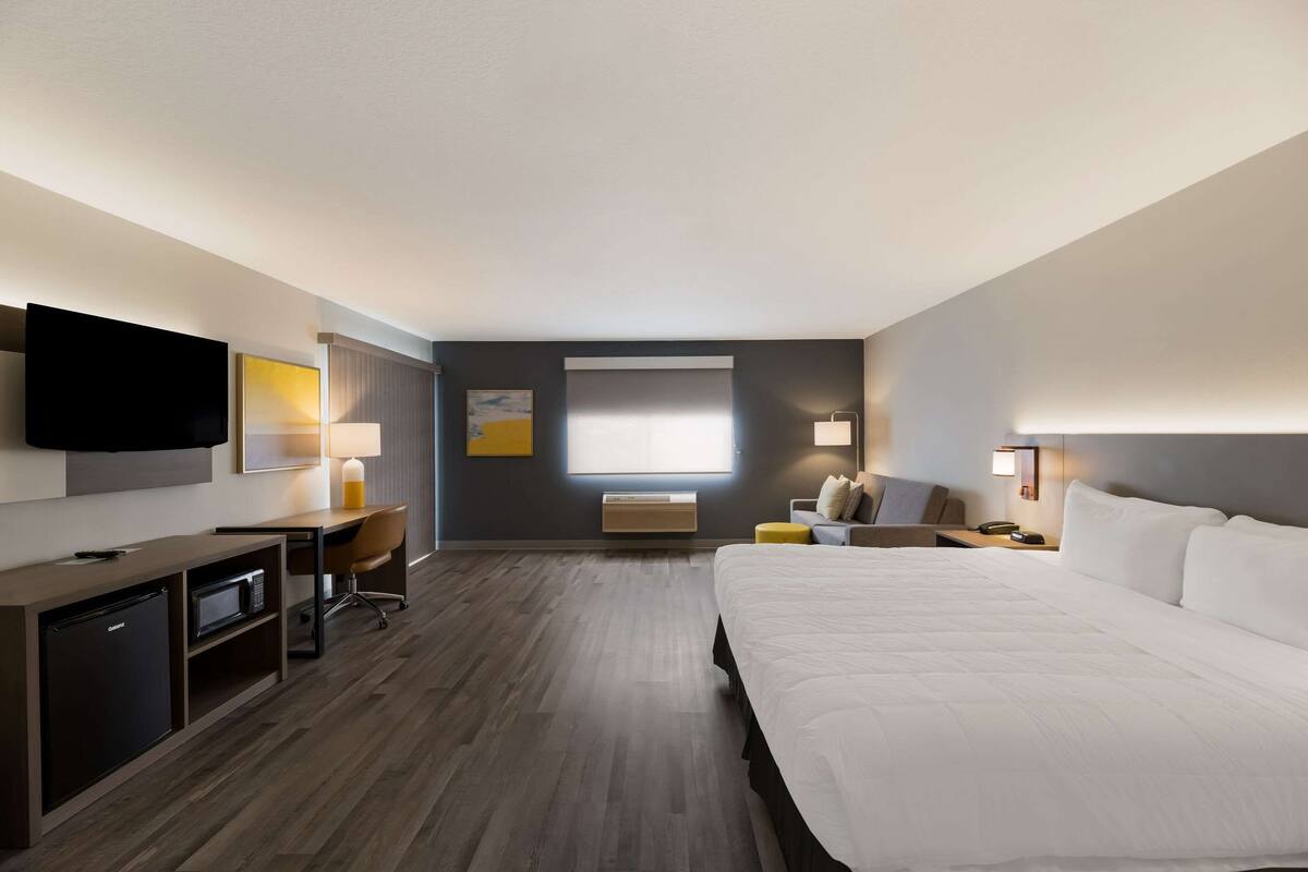 A hotel room with a large bed, a desk with a computer, a television, and a window with blinds.