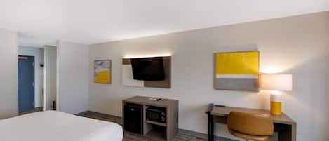 Habitación de hotel con cama, escritorio, silla, televisor y lámpara.