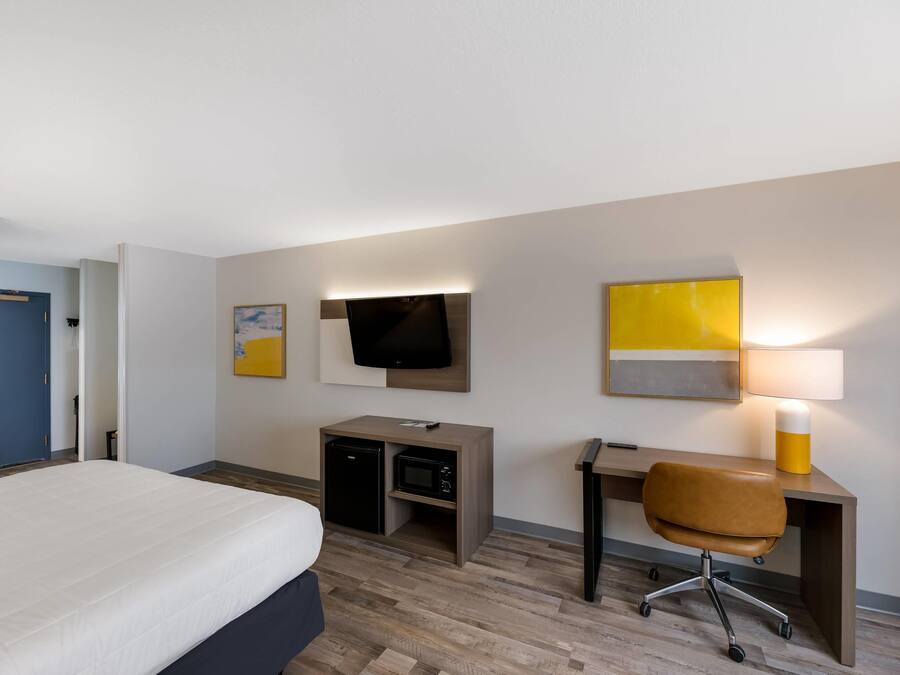 A hotel room with a bed, desk, chair, television, and a lamp.