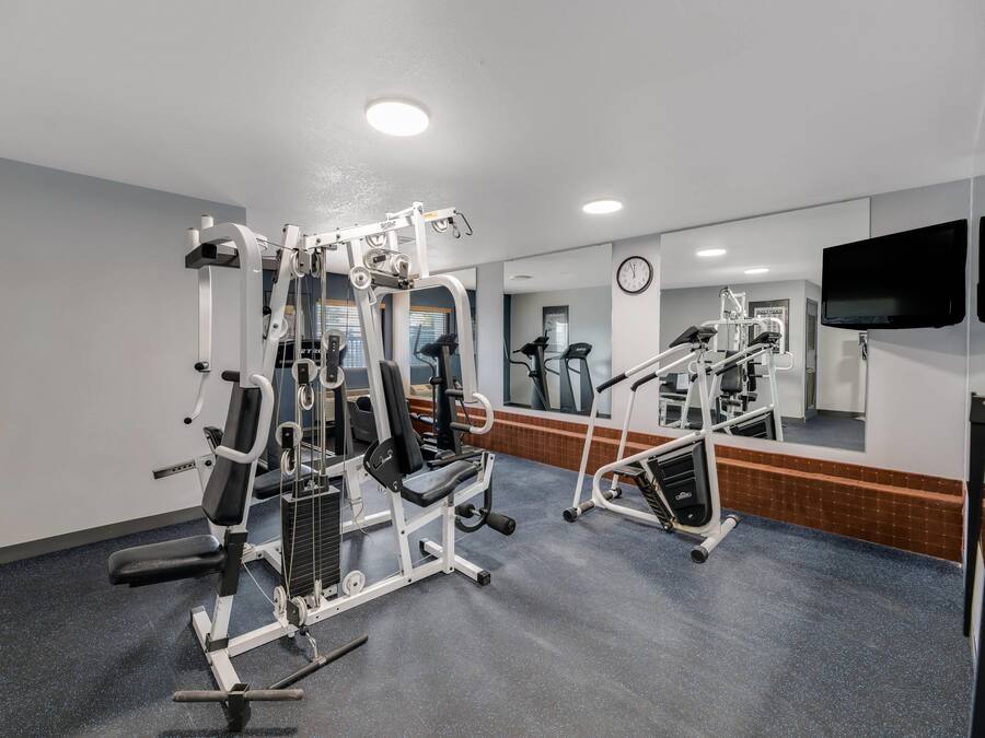 A gym with various exercise machines, a clock, and a television on the wall.