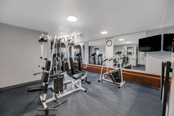 A gym with various exercise machines, a clock, and a television on the wall.