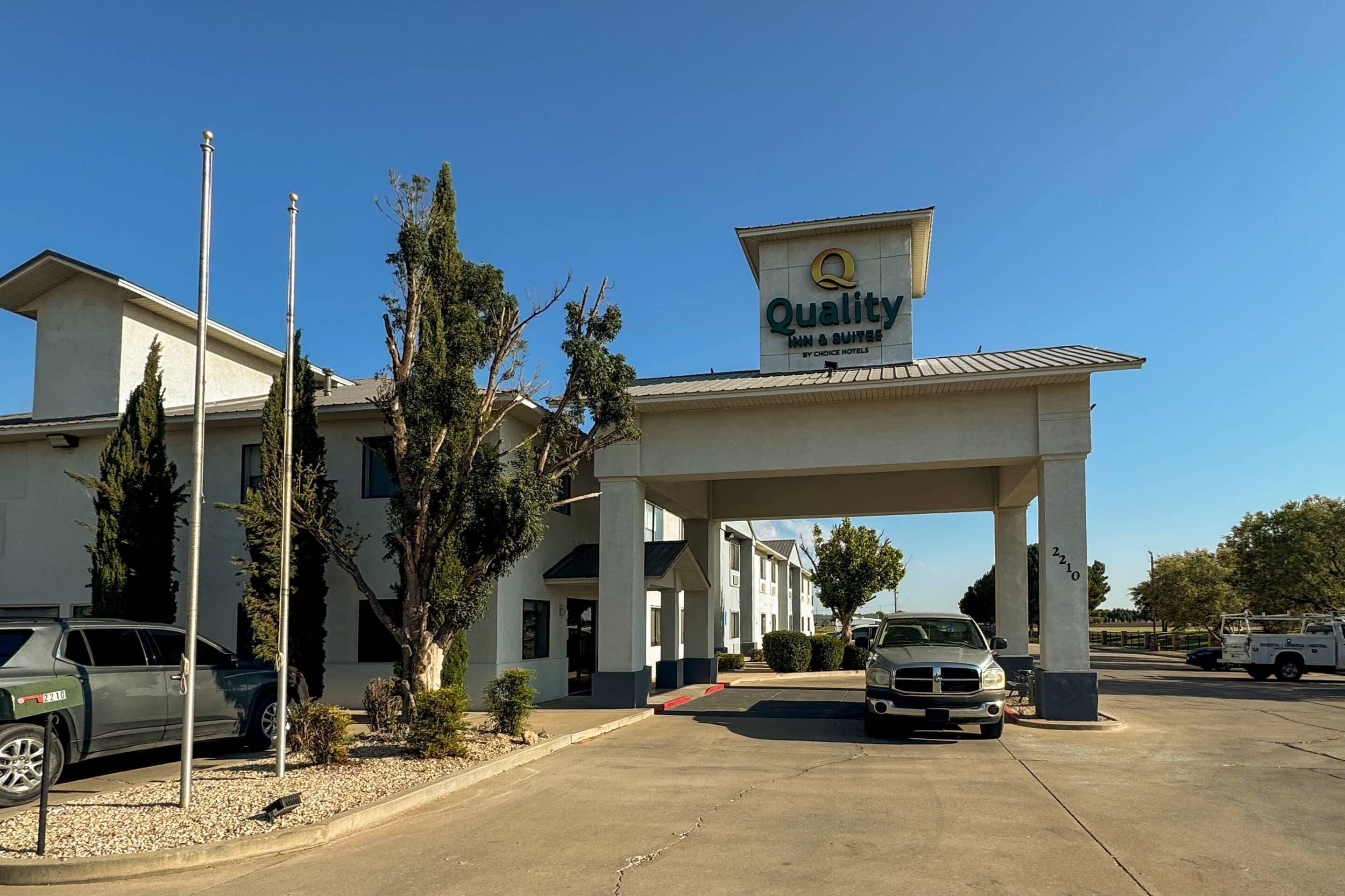 Un hôtel avec une enseigne indiquant « Quality Inn & Suites by Choice Hotels » et un parking où sont stationnés des véhicules.
