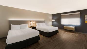 A hotel room with two beds, a nightstand, a lamp, a window with blinds, and a radiator.