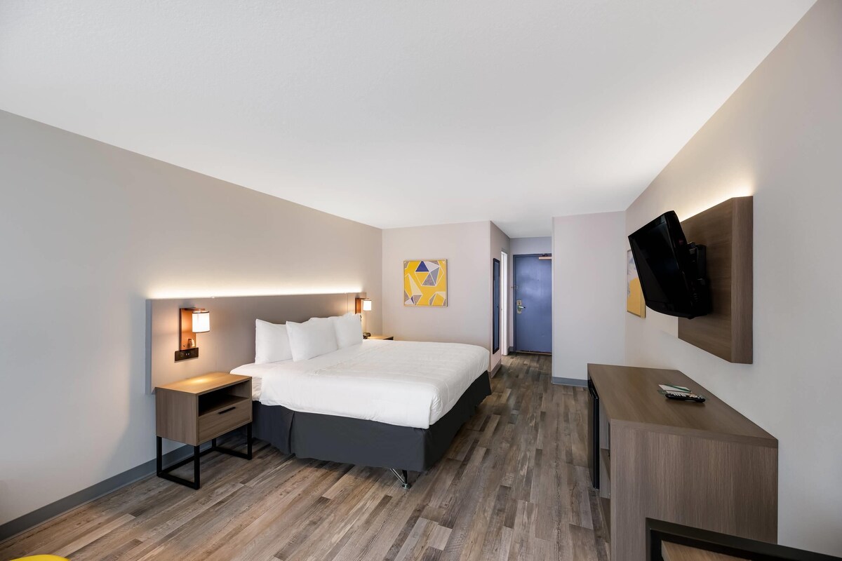 Ein Hotelzimmer mit Bett, Nachttischen, einem Schreibtisch, einem Fernseher und einer Tür zu einem weiteren Raum.