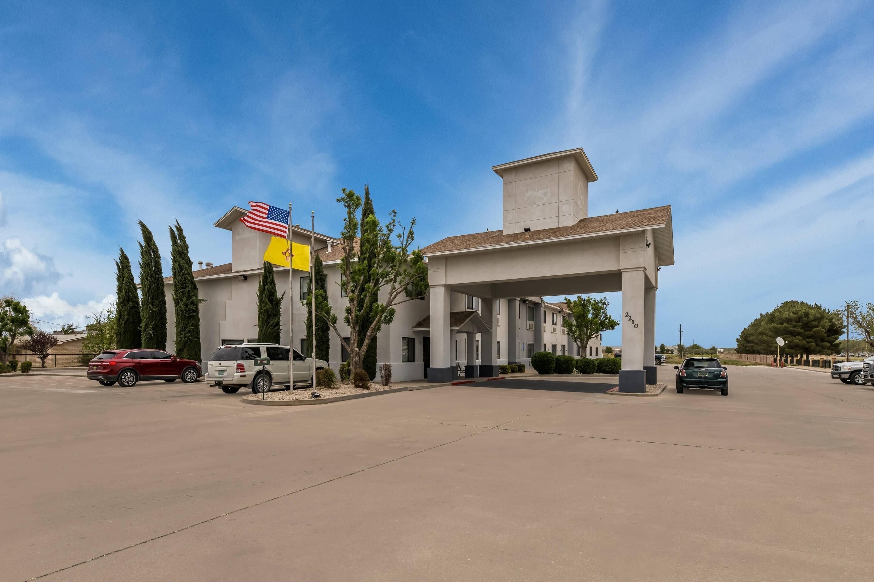 A building with a covered entrance and multiple windows, surrounded by parked cars and trees.