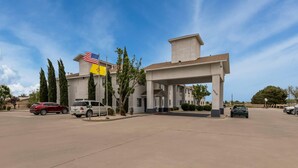A building with a covered entrance and multiple windows, surrounded by parked cars and trees. - Quality Inn & Suites Artesia (Artesia)