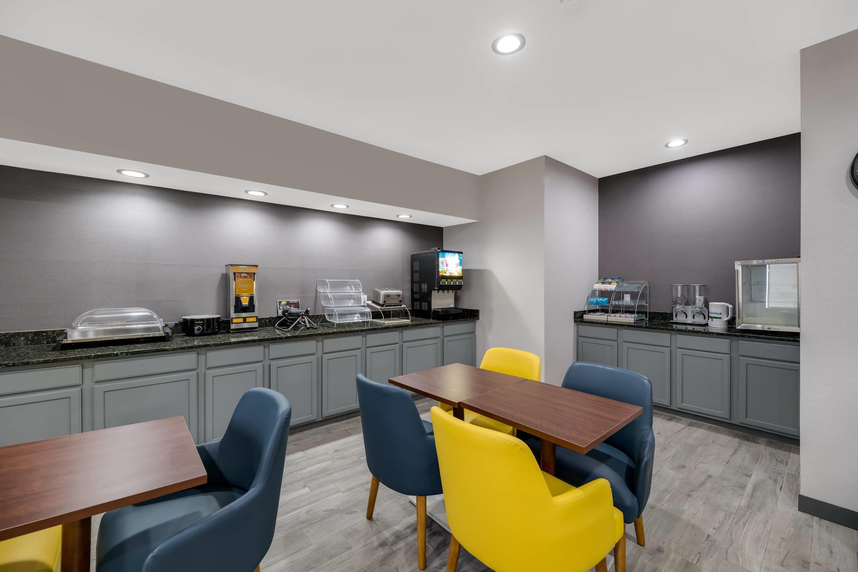 Habitación de hotel moderna con kitchenette, comedor con mesa y sillas, y un televisor de pantalla plana montado en la pared.