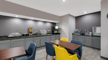 Habitación de hotel moderna con kitchenette, comedor con mesa y sillas, y un televisor de pantalla plana montado en la pared.