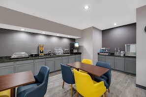 Une chambre d’hôtel moderne dotée d’une kitchenette, d’un coin repas avec une table et des chaises, et d’un téléviseur à écran plat fixé au mur.