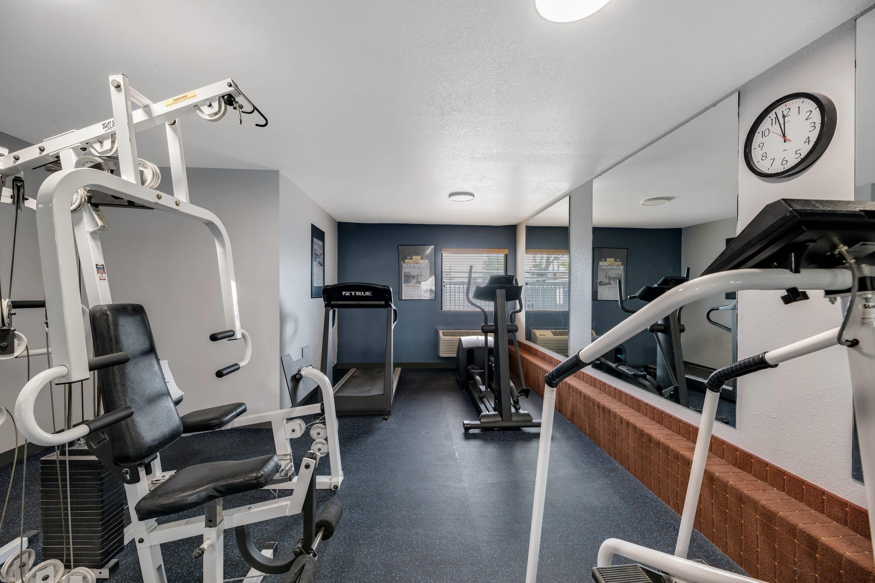 Un gimnasio con equipo de ejercicio diverso, una cinta de correr y un reloj en la pared.