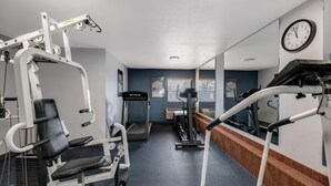Ein Fitnessstudio mit unterschiedlichen Trainingsgeräten, Laufbändern und einer Wanduhr.