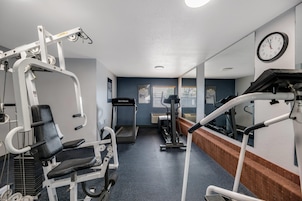 Un gimnasio con equipo de ejercicio diverso, una cinta de correr y un reloj en la pared.
