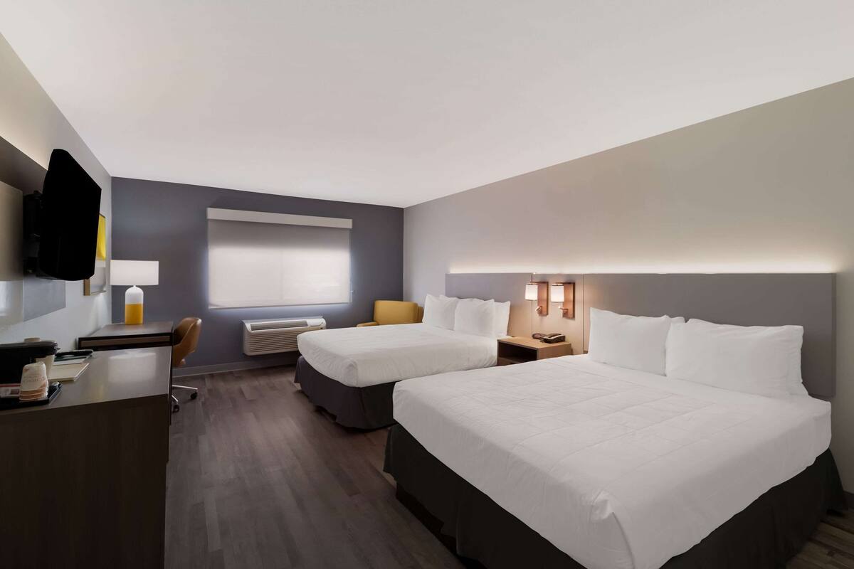 A hotel room with two beds, a desk, a chair, a TV, and a window with blinds.
