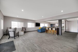 Amplia sala de estar con cocina, muebles grises y una zona de bar.