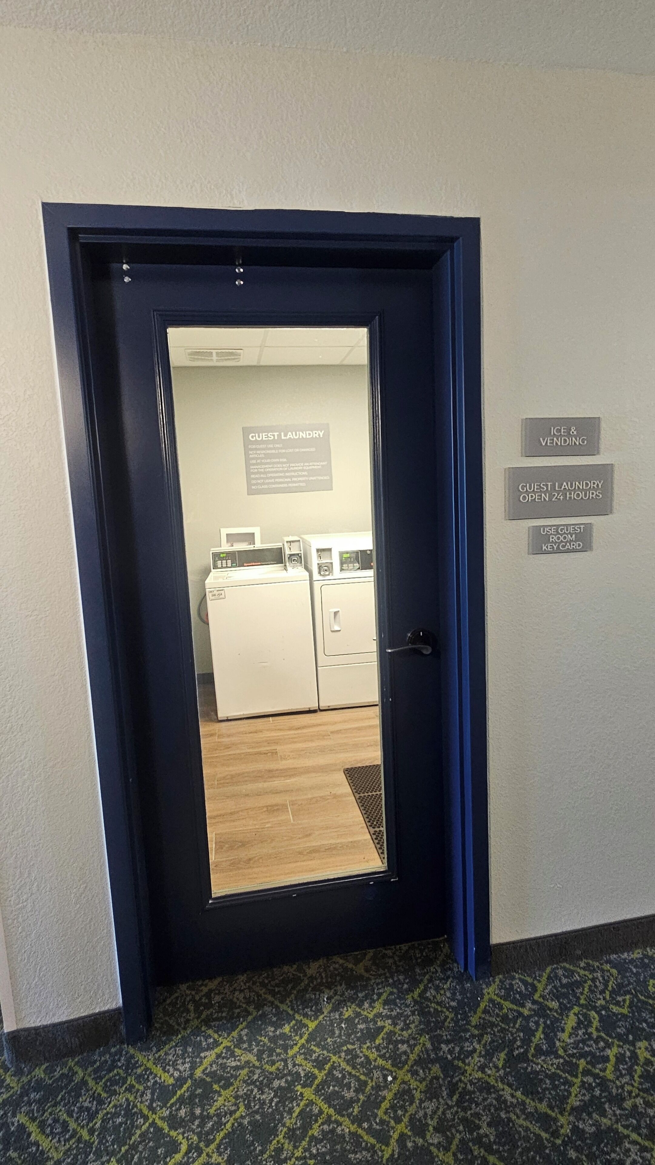 L’entrée d’une chambre d’hôtel donne sur une porte qui mène à une buanderie. Des panneaux indiquent la présence d’un service de blanchisserie pour les clients, d’un distributeur de glaçons et de boissons, ainsi qu’une option de blanchisserie ouverte 24 heures sur 24.