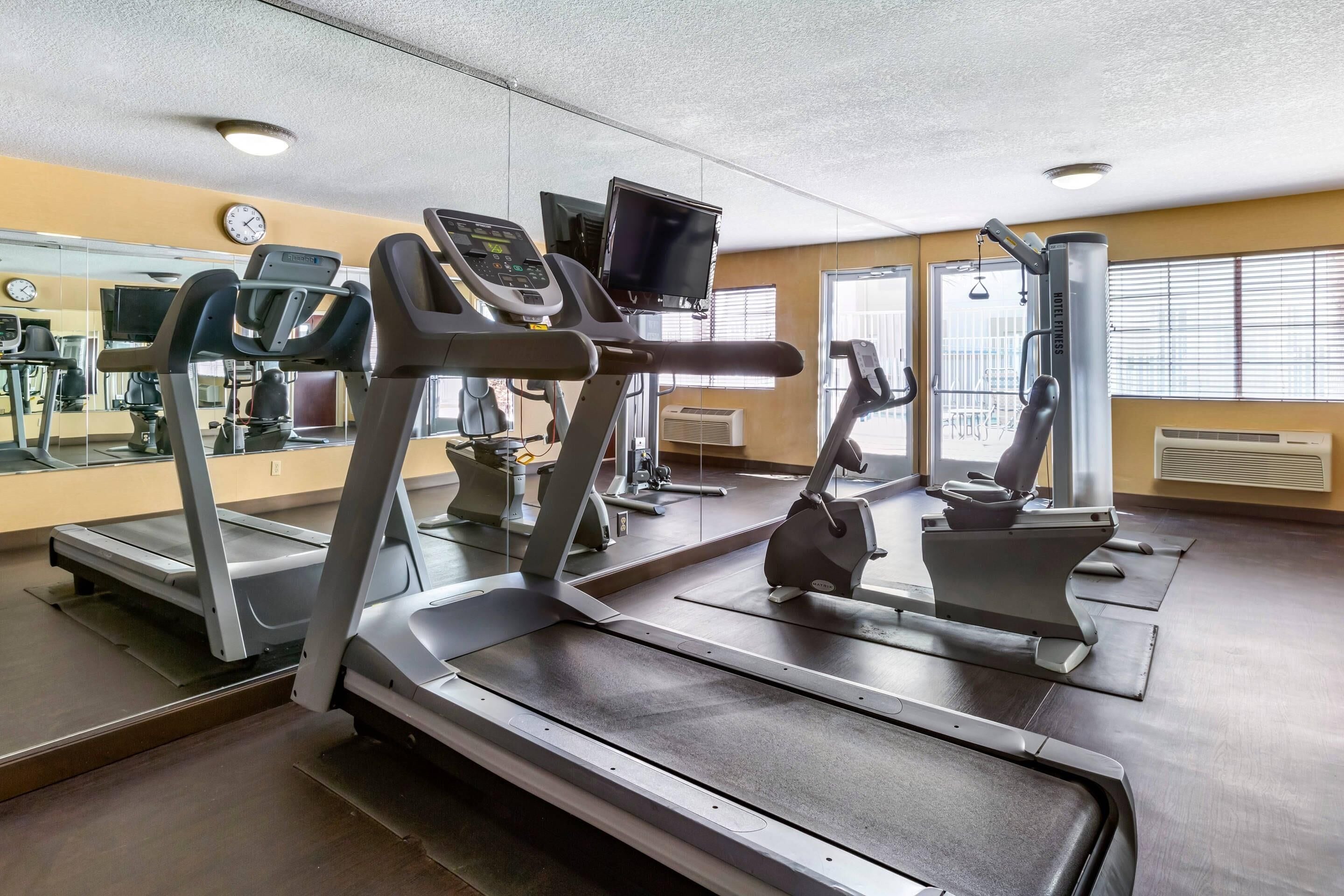 Une salle de sport équipée de tapis de course, de vélos d’exercice et d’un mur recouvert de miroirs.