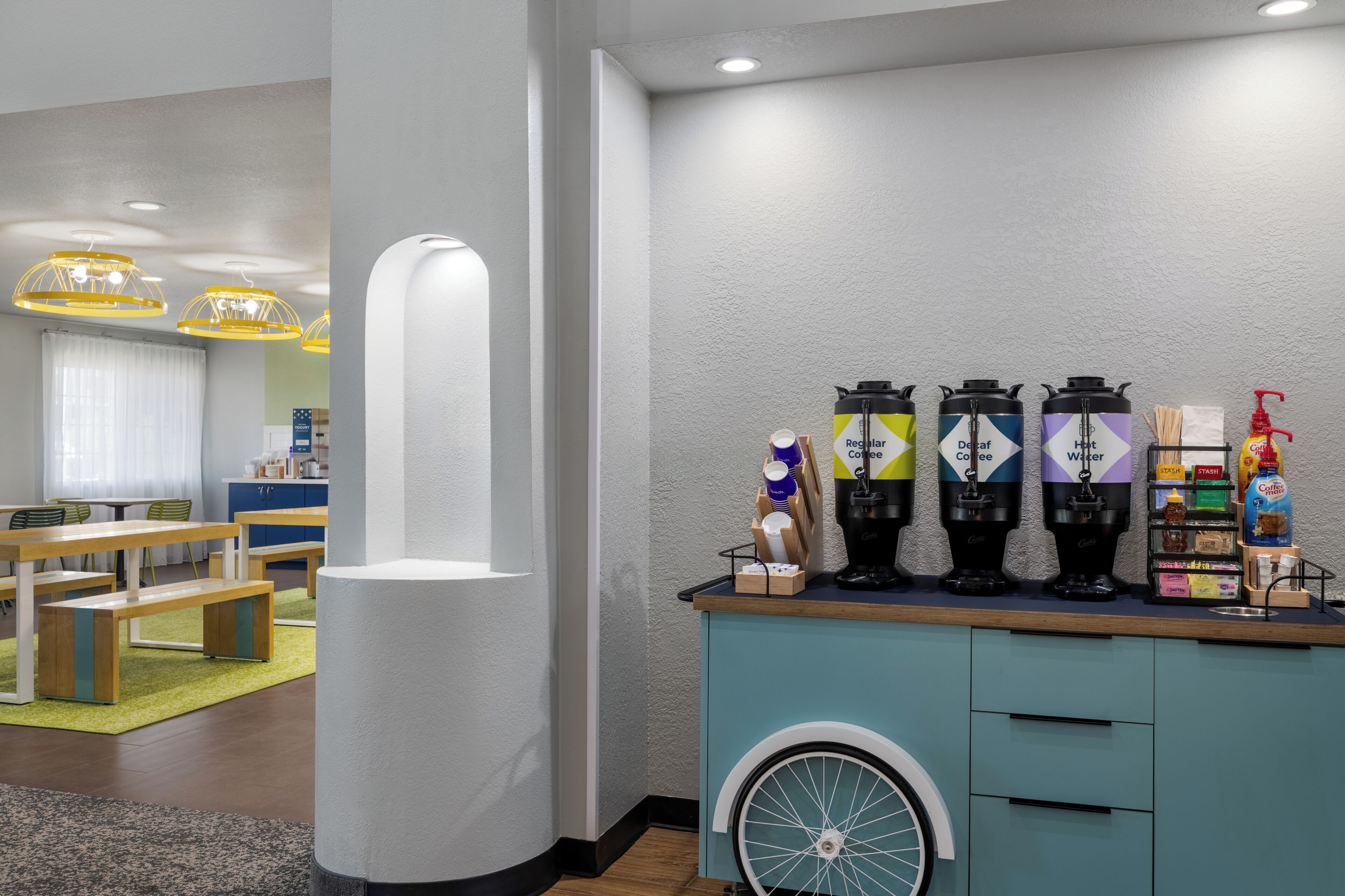 A modern coffee station with multiple coffee dispensers and a seating area with tables and chairs.