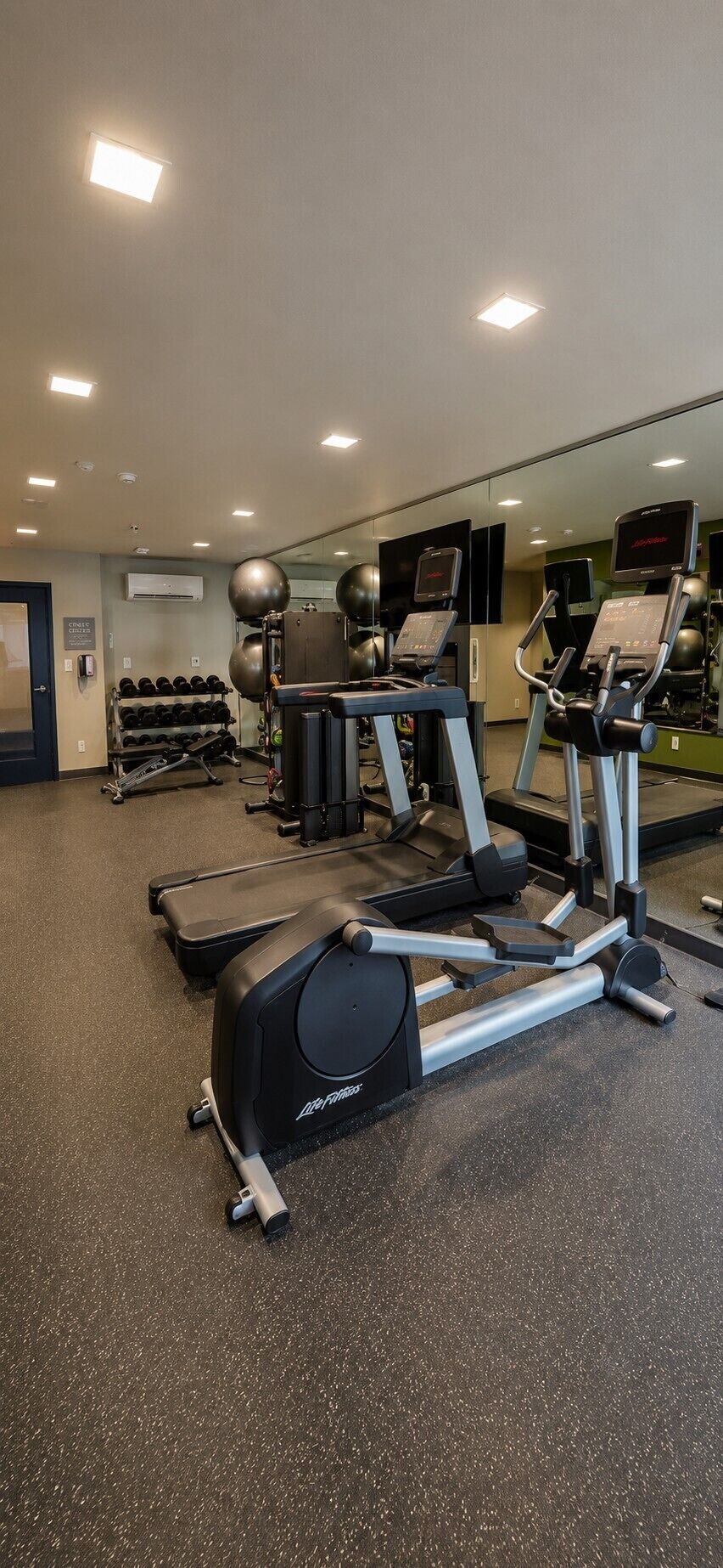 Un gimnasio con cintas de correr, elípticas y pesas libres.