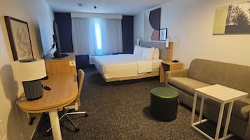 Una habitación de hotel con cama, escritorio, silla, sofá, una mesita y un otoman verde.