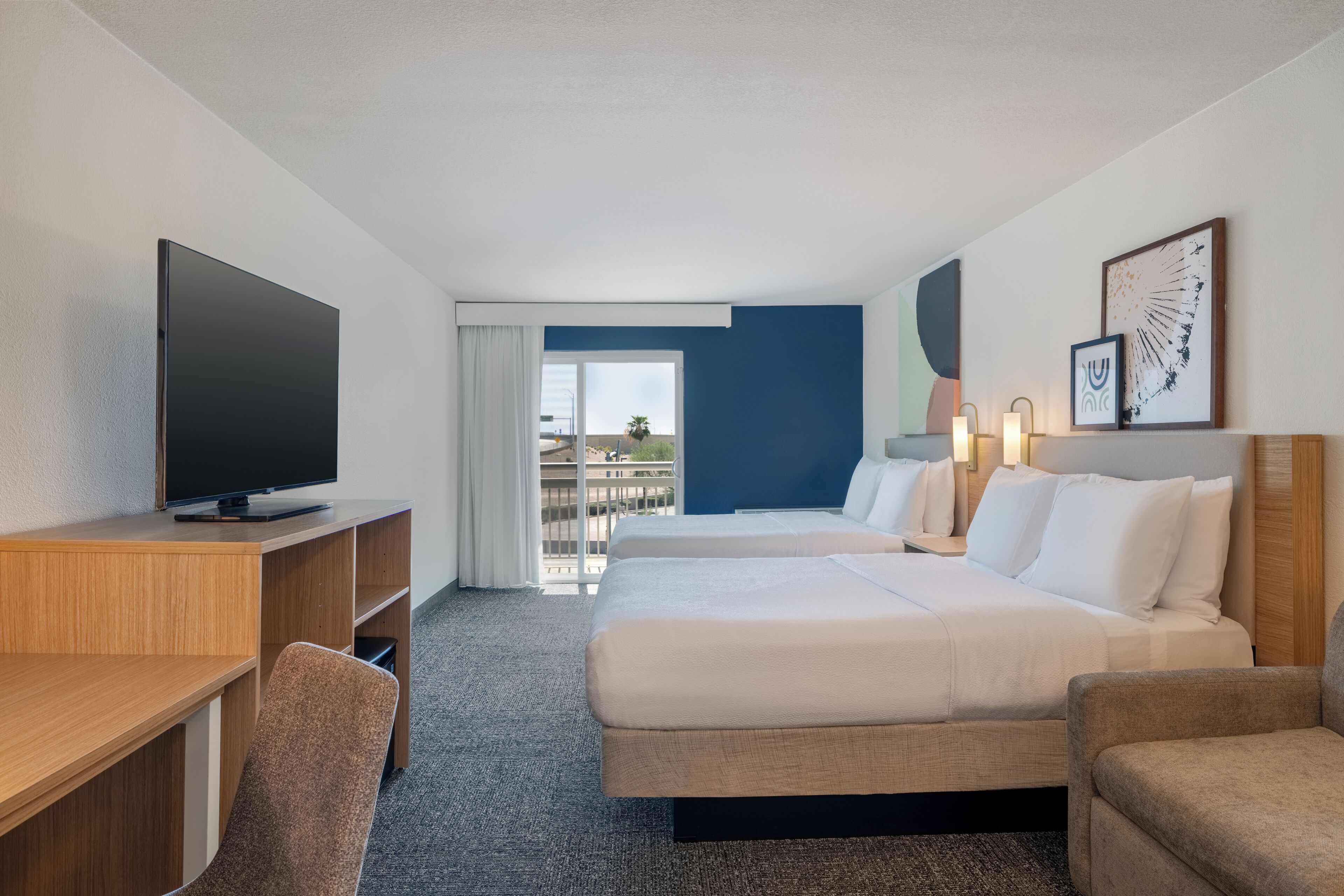 A hotel room with a large flat-screen TV, two beds, a desk, and a chair.