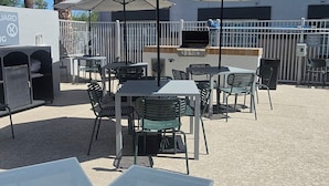 Outdoor seating with umbrellas, a grill, and a building with barred windows. - Spark by Hilton Tempe Phoenix Airport (Tempe)
