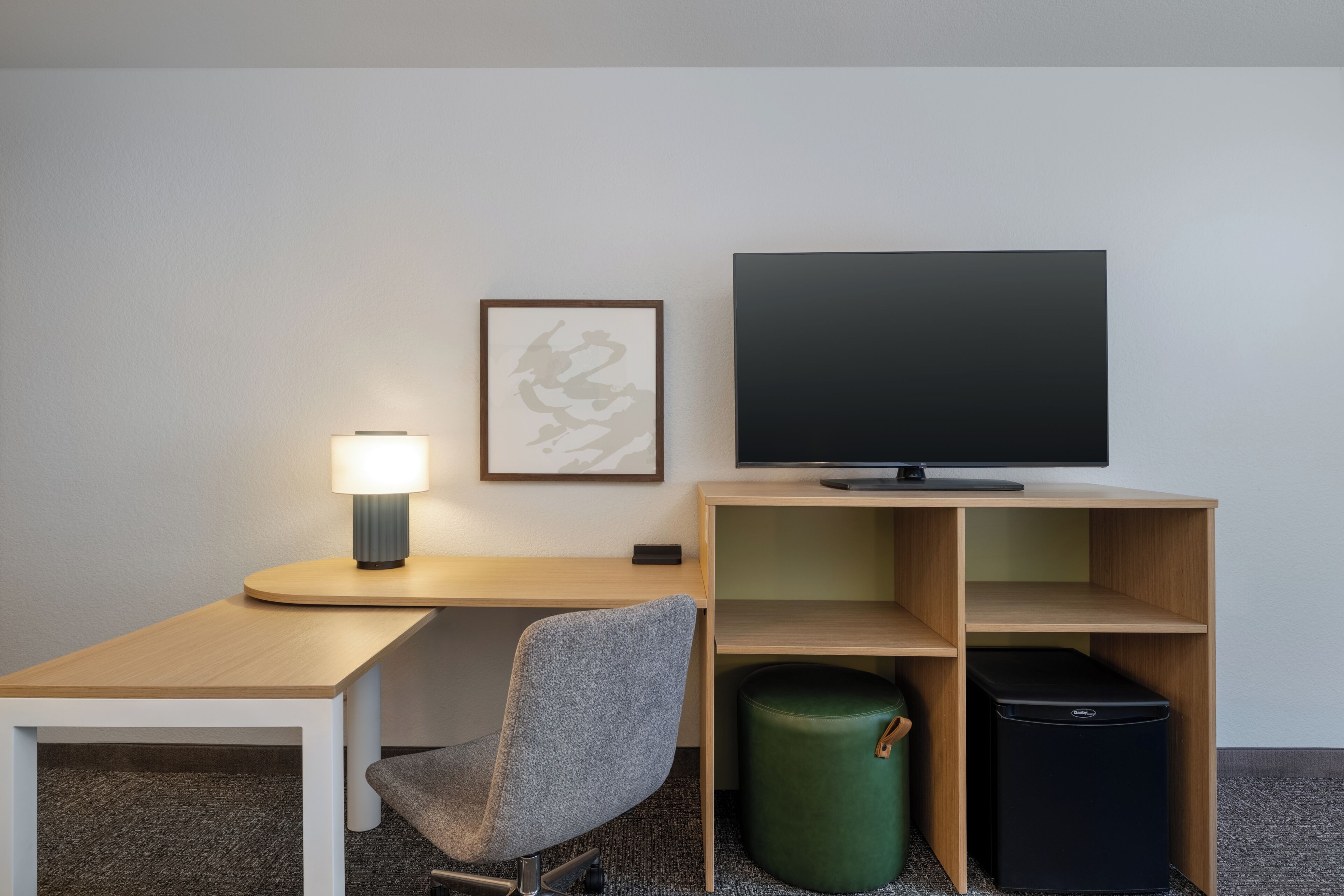 A hotel room with a desk, chair, television, lamp, and a trash bin.