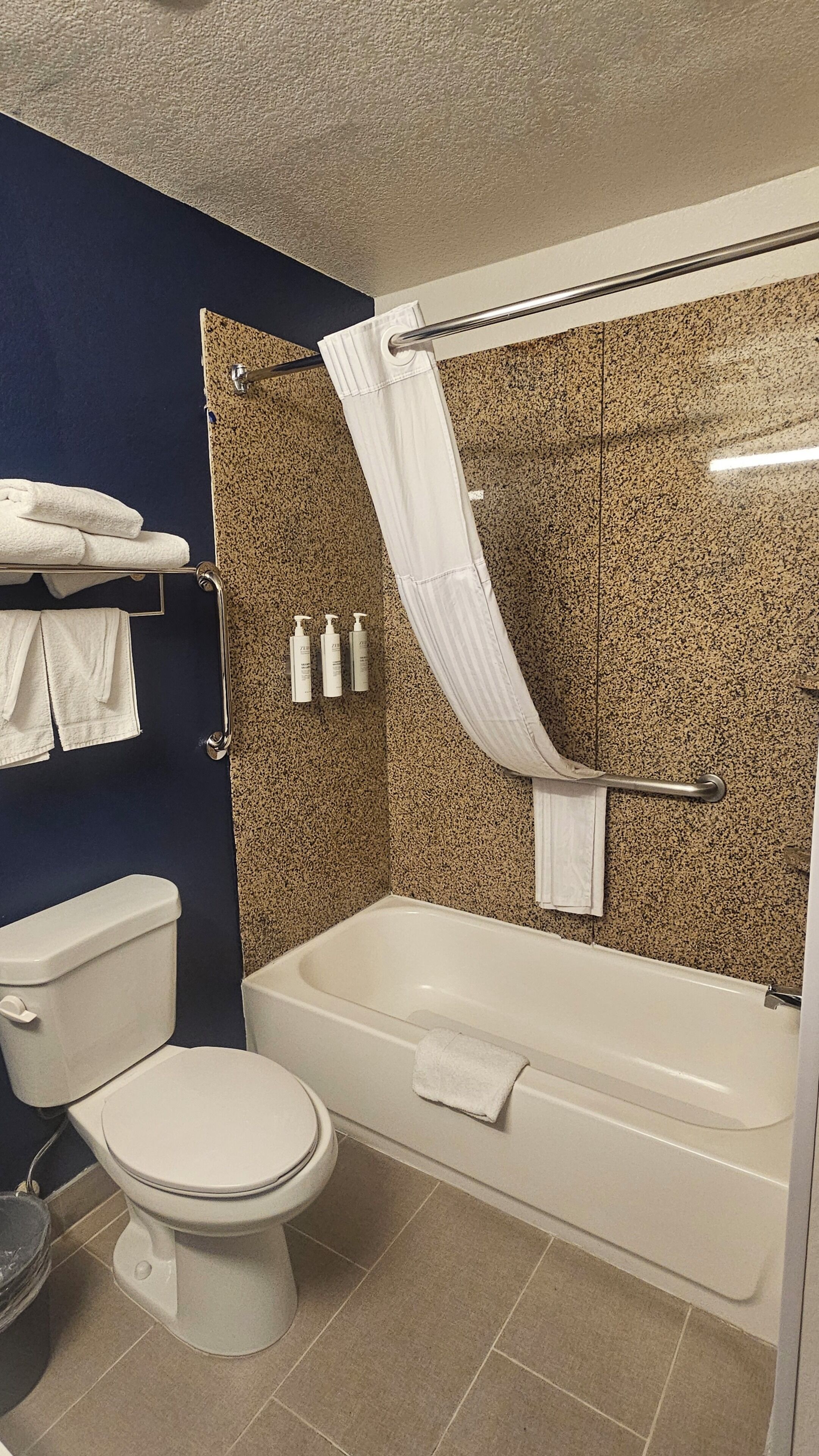 A bathroom with a toilet, bathtub, shower curtain, towel rack, and toiletries.