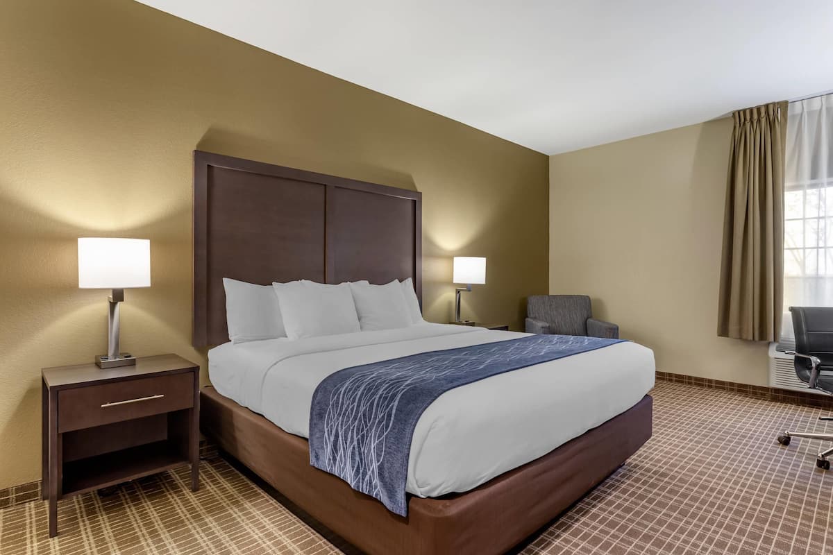 A hotel room with a large bed, two bedside lamps, a chair, and a window with curtains.