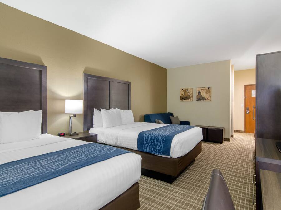 A hotel room with two beds, a desk, a TV, and a lamp.