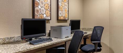 Un espacio de trabajo en hotel con dos monitores, una impresora y dos sillas de oficina.