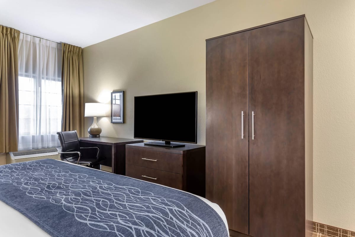 A hotel room with a bed, a desk with a TV, a wardrobe, and a chair.