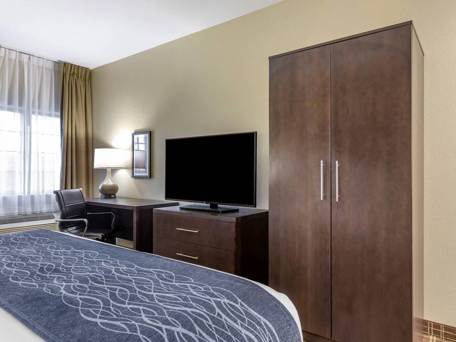 A hotel room with a bed, a desk with a TV, a wardrobe, and a chair.