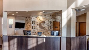 A reception area with a stone wall, a flat-screen TV, and a reception desk with a phone and a computer. - Comfort Inn St. Robert / Fort Leonard Wood (St. Robert)